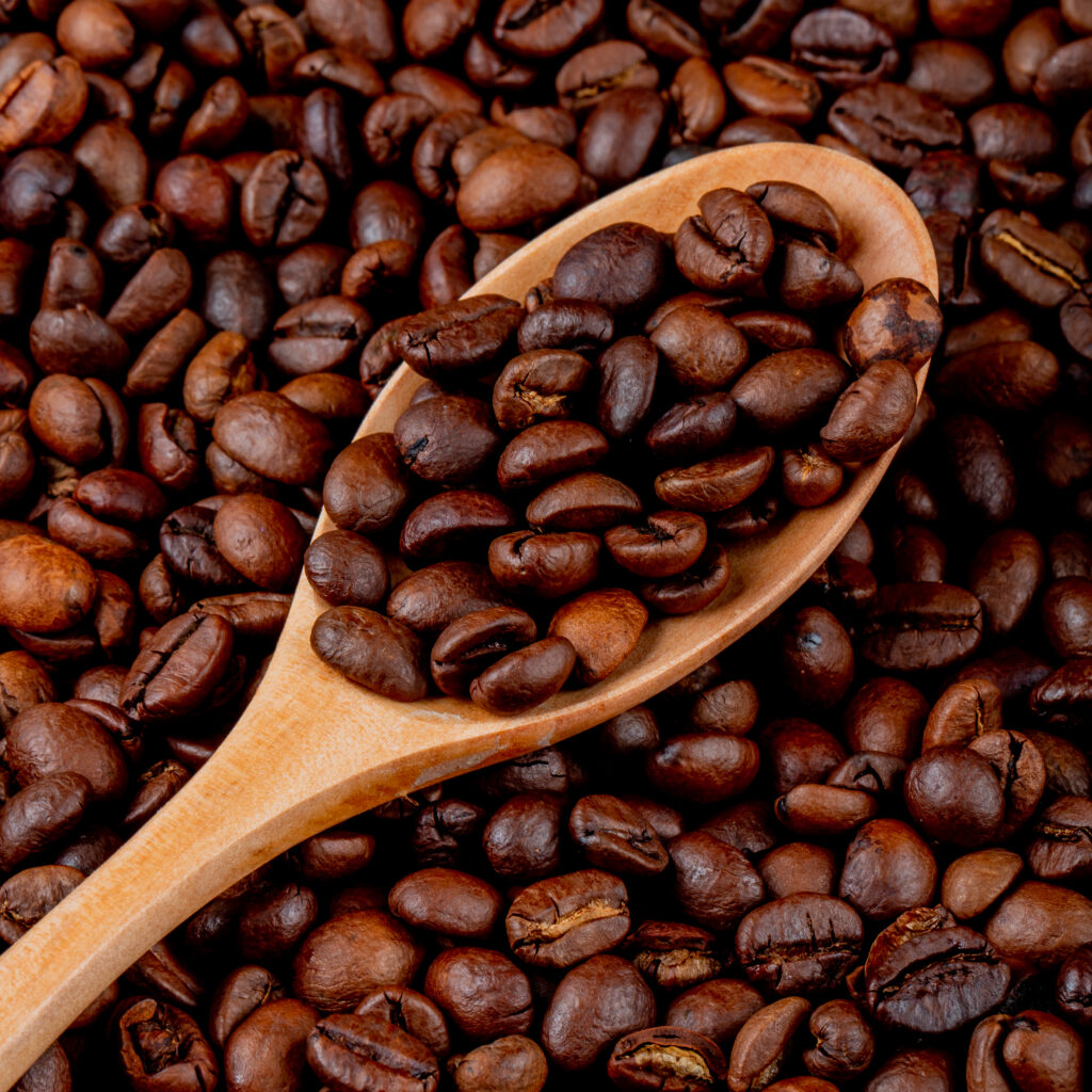 coffee beans in a wooden spoon on coffee beans background top view